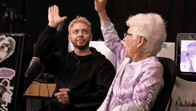 a man and an older woman are giving each other a high five while sitting in front of a microphone .