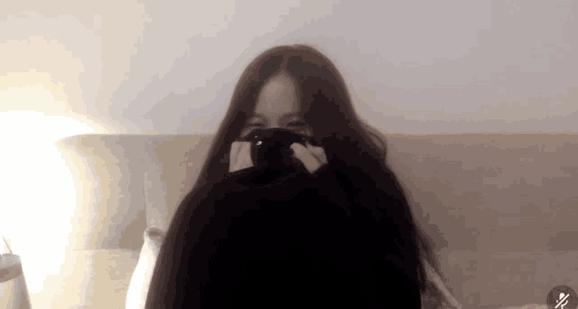 a woman covering her face with a black sweater with a x on it