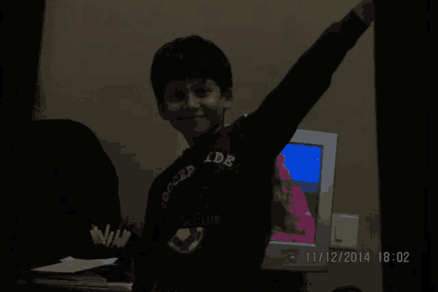 a boy wearing a shirt that says forced ide is standing in front of a computer monitor