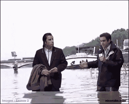 a man in a suit is standing in the water while a man in a jacket is standing in the water .