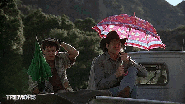 a man in a cowboy hat sits in the back of a truck holding an umbrella with tremors written on the bottom