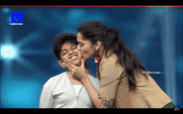 a woman kisses another woman on the cheek in front of a television screen that says mallemala tv