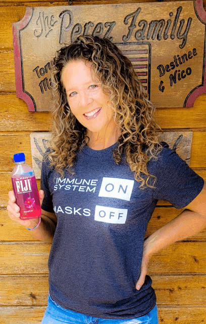 a woman wearing a shirt that says immune system on masks off holds a bottle of fiji