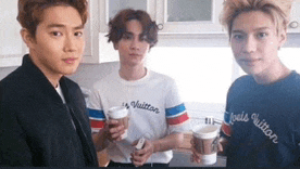 three young men are standing next to each other in a kitchen holding coffee cups .