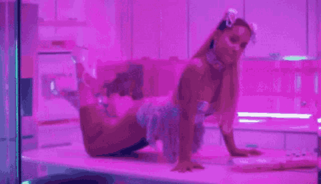 ariana grande is laying on her stomach on a table in a kitchen .