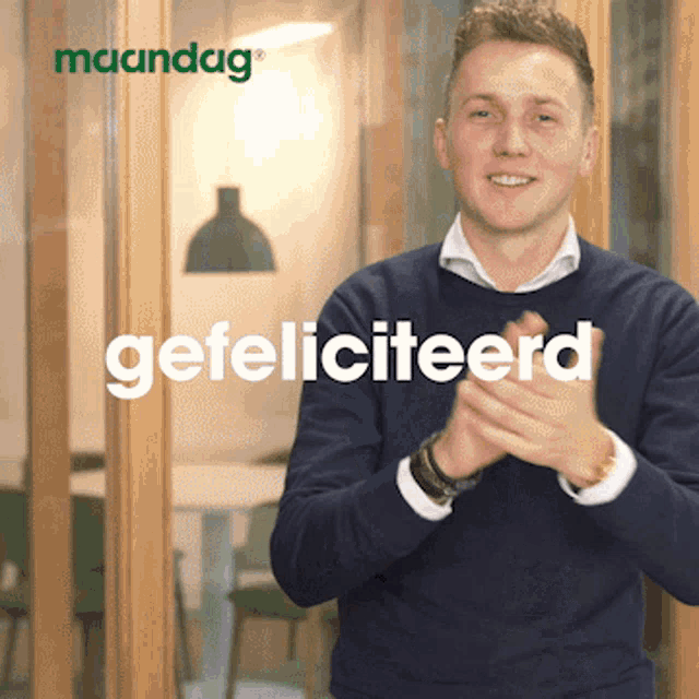 a man in a blue sweater is clapping in front of a sign that says gefeliciteerd