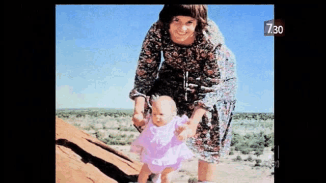 a woman in a floral dress is holding a baby in her arms and the time is 7:30