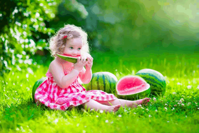 a little girl is eating a slice of watermelon while sitting in the grass