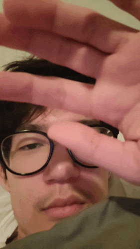 a man wearing glasses is covering his face with his fingers