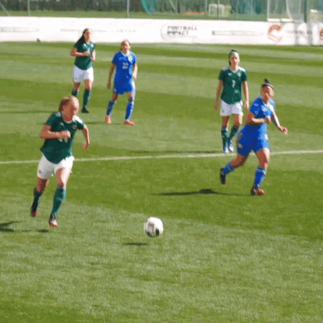 a group of female soccer players are playing on a field with a sign that says " football for all "