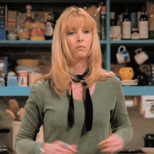 a woman wearing a green shirt and a black tie is standing in front of a shelf full of food items .