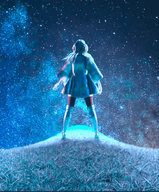 a woman standing on top of a grassy hill looking up at the stars