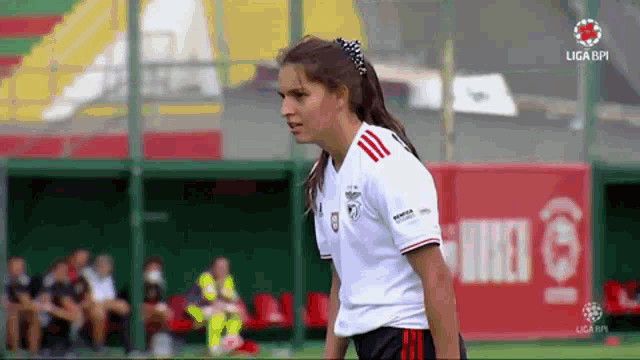 a female soccer player stands on the field in front of a sign that says ' liga ' on it