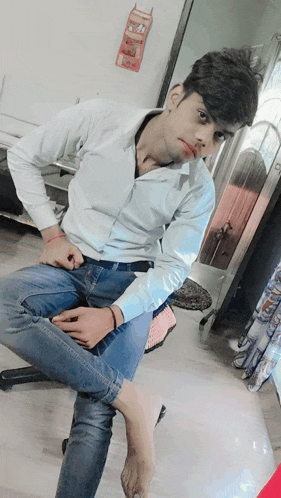 a young man in a white shirt and blue jeans sits on a stool