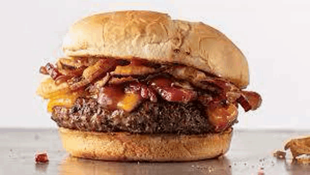 a close up of a hamburger with bacon , cheese and onions on a table .