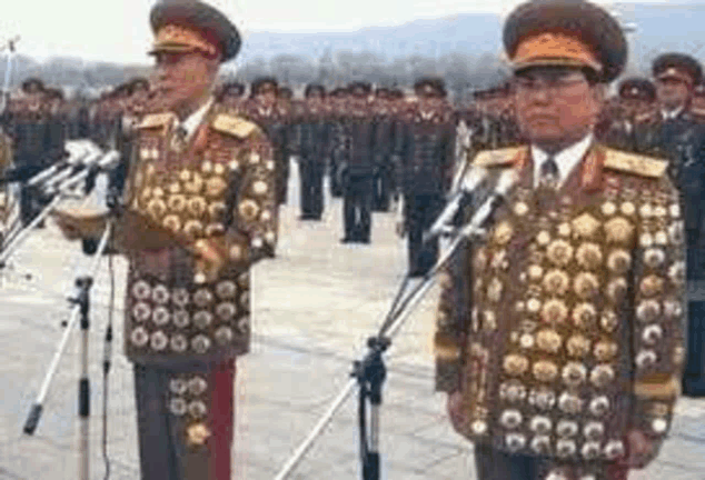 two military men are standing in front of microphones in front of a crowd of soldiers .