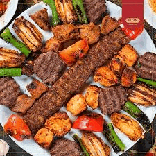 a white plate topped with a variety of meats , vegetables and shish kebabs .