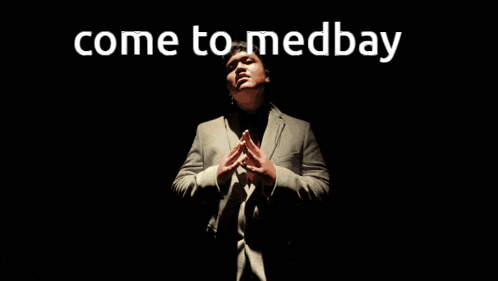 a man in a suit stands in a dark room with the words come to medbay behind him