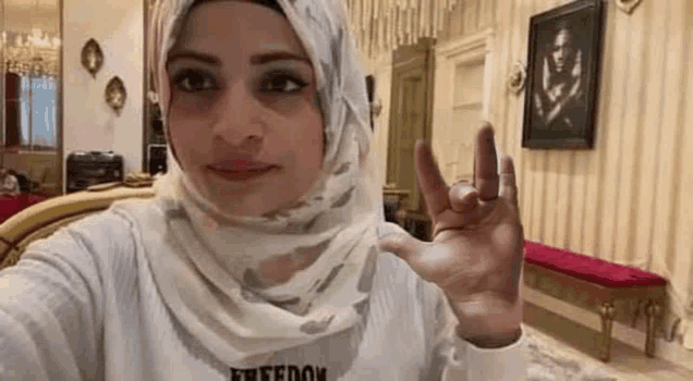 a woman in a hijab is taking a selfie in a living room with her hand up .