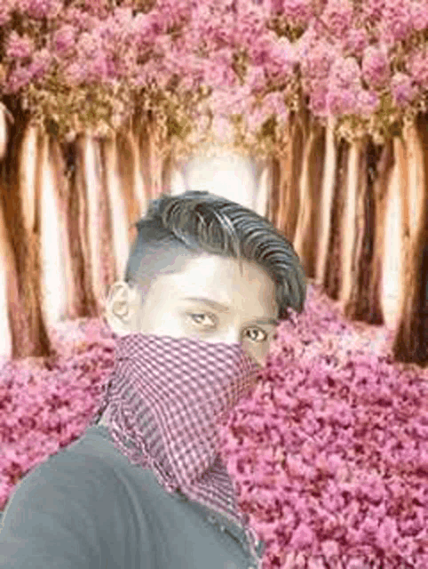 a young man wearing a scarf around his face is standing in front of a forest of pink flowers .