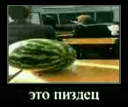 a watermelon is sitting on a table in a classroom with people sitting at desks in the background .