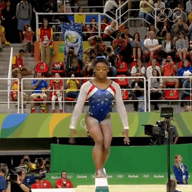 a female gymnast is doing a trick on a balance beam in front of a crowd at the rio2016 olympics