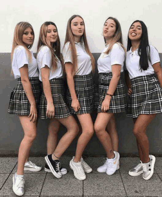 a group of girls wearing plaid skirts and white shirts pose for a photo