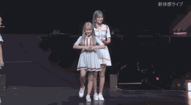 two girls with blue hair are dancing on a stage in front of a sign that says 新体 感 ライブ