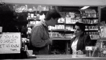 a black and white photo of a man and woman in a store with a sign that says if you plan to shoplift let us know thanks