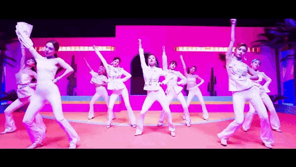 a group of women in white pants are dancing in front of a purple wall with a sign that says j.