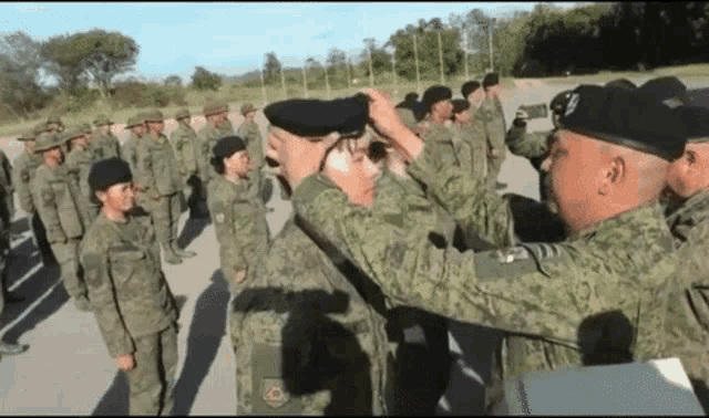 a group of soldiers are standing in a line and one of them is wearing a hat with the letter c on it .