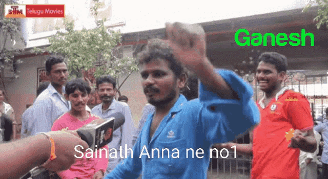 a man in a blue shirt is being interviewed by a person with a microphone in front of a sign that says ganesh