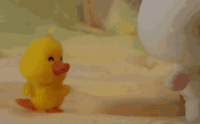 a small yellow rubber duck with a red beak is walking on a bed