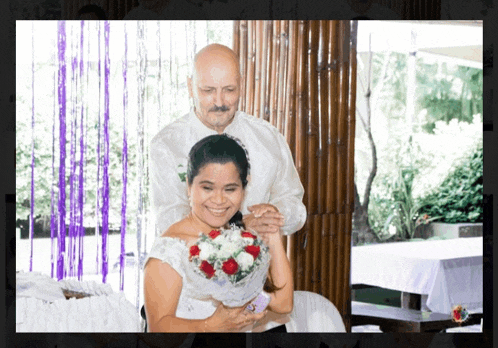 a bride and groom are posing for a picture and the bride is holding a bouquet of red and white roses