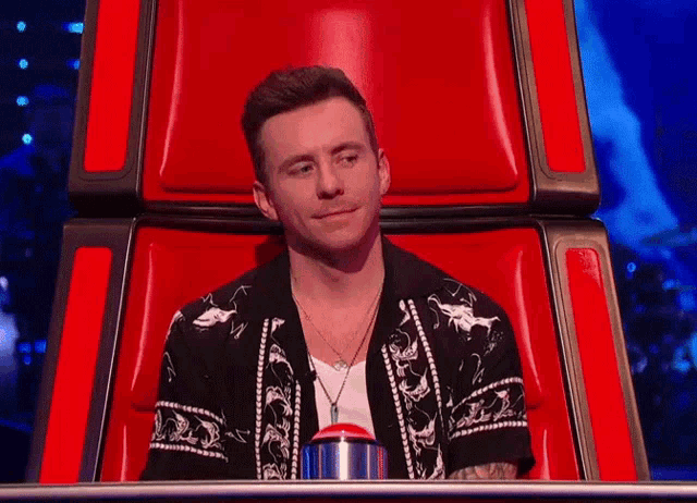 a man in a black and white shirt sits in a red chair with a button in front of him