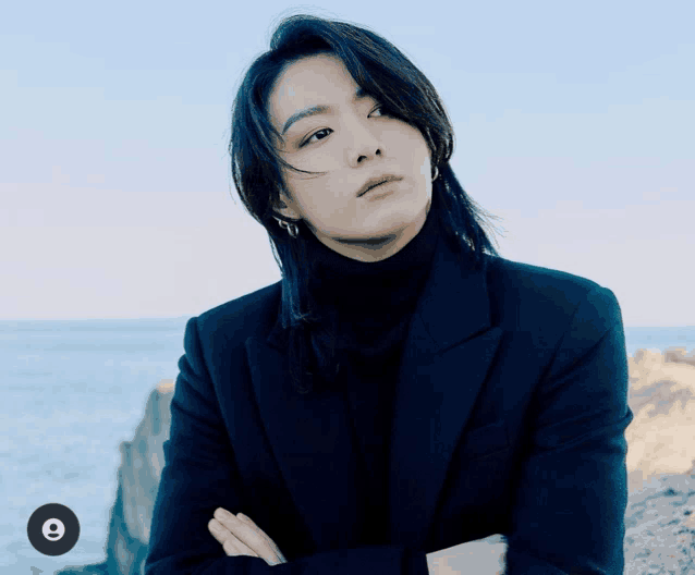 a man with long hair wearing a black jacket and turtleneck