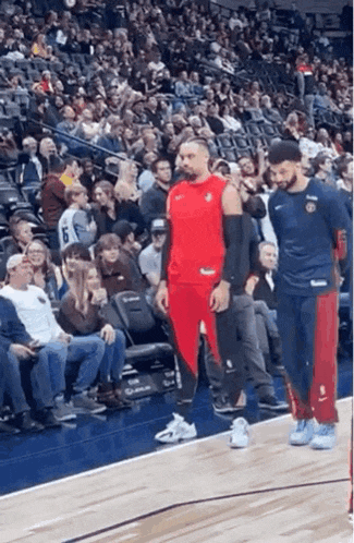 a man in a red shirt and red pants is standing on a basketball court in front of a crowd .