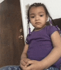 a little girl wearing a purple shirt is sitting on a bed .