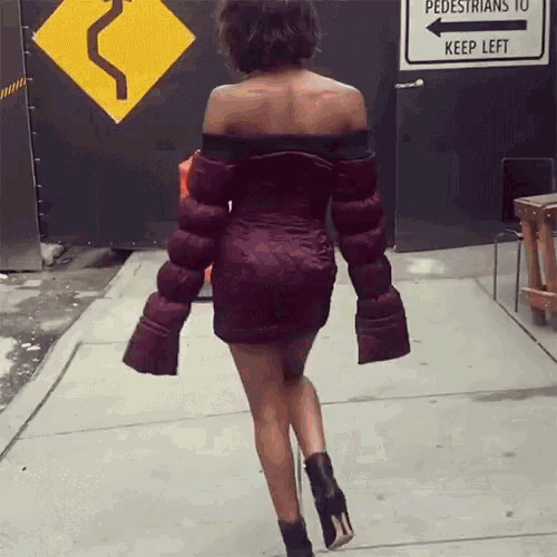 a woman in a red dress is walking down a sidewalk in front of a sign that says pedestrians to keep left