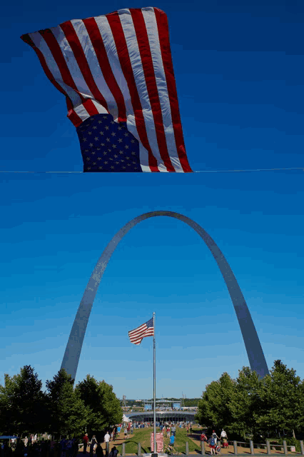 a large american flag is flying in front of a large arch