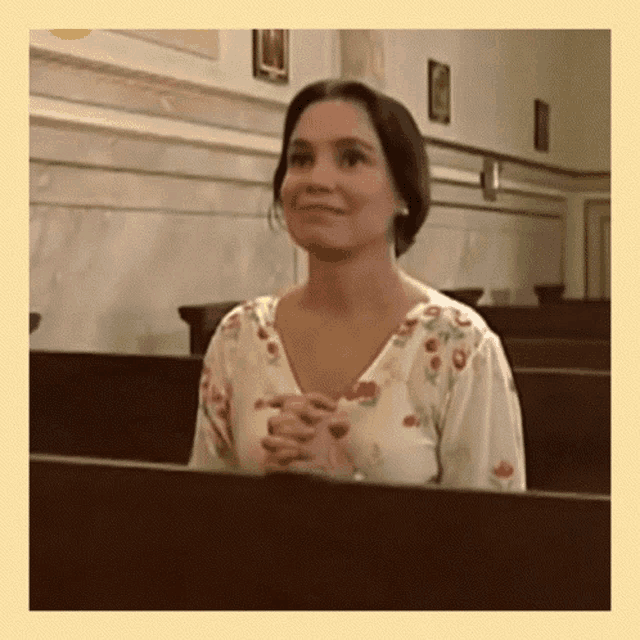 a woman is sitting in a church with her hands folded and smiling