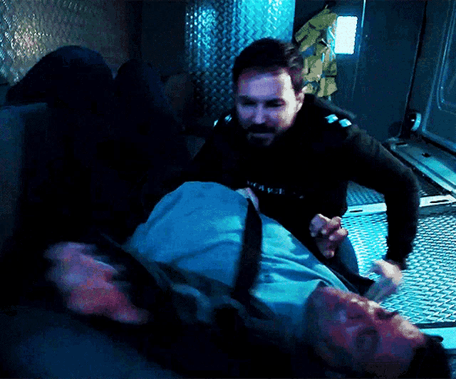 a man in a black shirt with the word police on it is holding another man laying on the floor