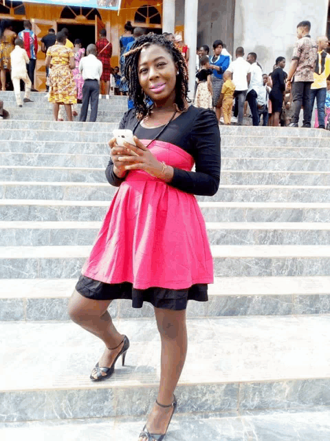 a woman in a pink dress is standing on stairs holding a cell phone