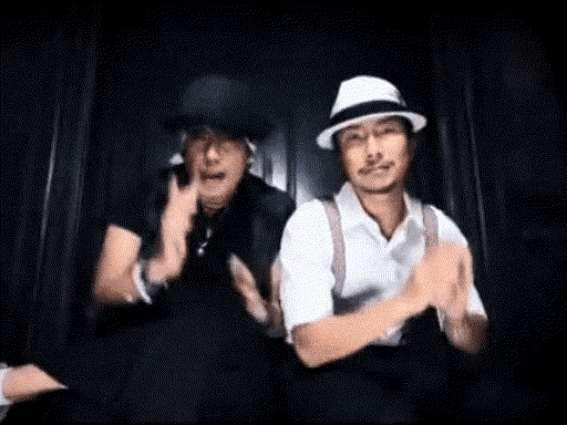 two men wearing hats are clapping their hands in a dark room .