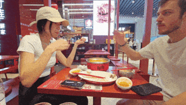 a man and a woman are sitting at a table with plates of food and a phone that says 50