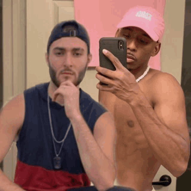 a shirtless man is taking a selfie in front of a mirror with another shirtless man .