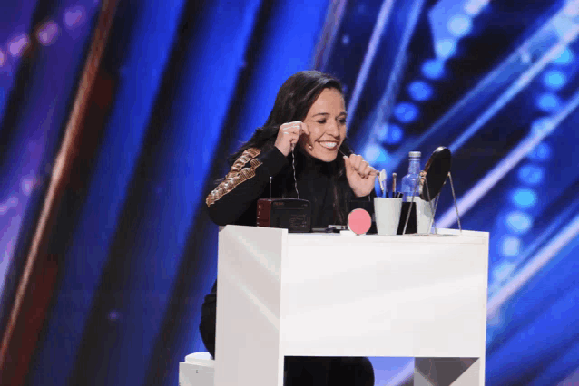 a woman is sitting at a table with a bottle of water and a mirror