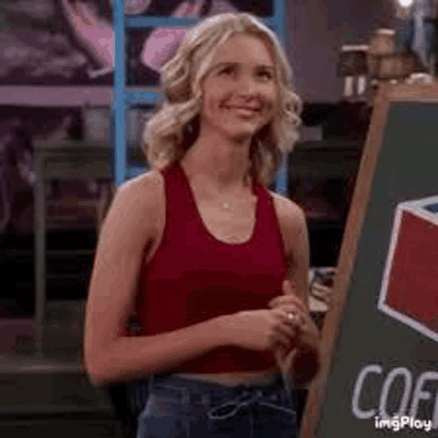 a woman in a red tank top is standing next to a blackboard .