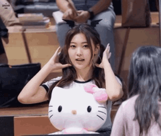 a girl is holding a hello kitty stuffed animal and wearing a bat headband .