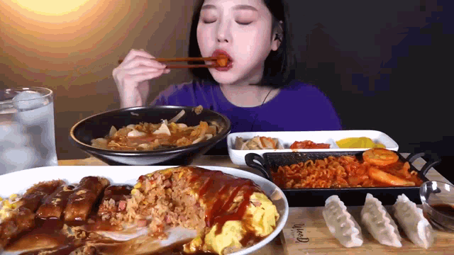 a woman is eating food with chopsticks while sitting at a table with plates of food and a glass of water